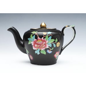 May include: A black teapot with a floral design. The teapot has a gold knob on the lid and a white handle. The flowers are pink, blue, yellow, and green.