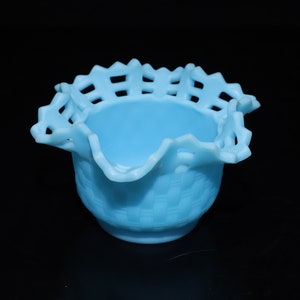May include: A light blue glass bowl with a ruffled edge and a woven pattern. The bowl is made of milk glass and has a delicate, feminine look.
