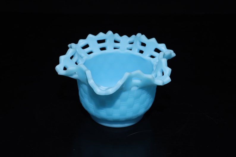 May include: A light blue glass bowl with a ruffled edge and a woven pattern. The bowl is made of milk glass and has a delicate, feminine look.