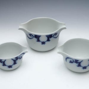 May include: Three white ceramic bowls with blue floral designs. The bowls are nested inside each other, with the largest bowl at the top and the smallest bowl at the bottom.