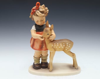 May include: A porcelain figurine of a young girl in a red dress and a black top, with a red bow in her hair, gently holding a fawn. The fawn has white spots and is standing on a beige base.