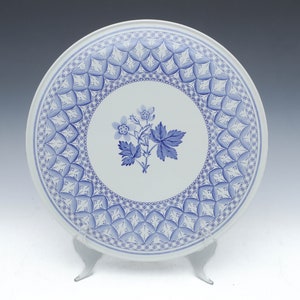 May include: A white ceramic plate with a blue and white floral design. The plate has a decorative border with a repeating pattern of blue and white geometric shapes.