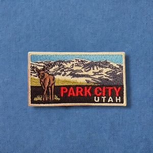 May include: Embroidered patch with a brown moose standing in front of a mountain range. The patch has a white border and says "Park City, Utah" in red text.