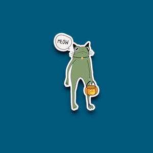 May include: A green frog wearing a black collar and holding a small orange pumpkin bucket. A speech bubble above the frog says "MEOW".