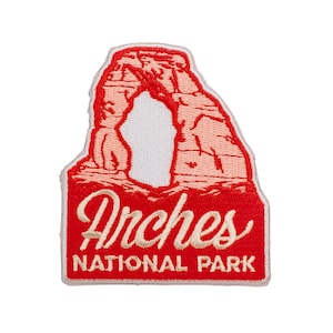May include: Embroidered patch featuring a red and peach-colored depiction of a rock archway. The patch has the words "Arches NATIONAL PARK" in a white, cursive font on a red background. The patch is rectangular with rounded corners.