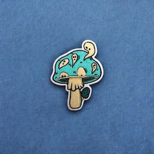 May include: A blue and green mushroom with a white stem and a yellow top. The mushroom has a cartoon-like face and is surrounded by small white ghosts.