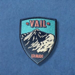 May include: A blue and white embroidered patch with the text "Vail, Colorado" and a mountain scene.