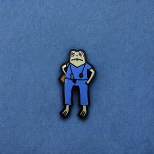 May include: A green frog wearing blue scrubs and a stethoscope. The frog is standing with its arms crossed and has a serious expression on its face.
