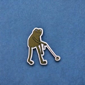 May include: A green frog with a white stick in its hand, walking a brown ball on a blue background.