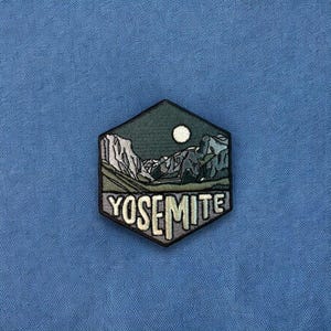 May include: A hexagonal embroidered patch with a dark green, gray, and white mountain scene and a white moon. The text "Yosemite" is embroidered in white on the patch.
