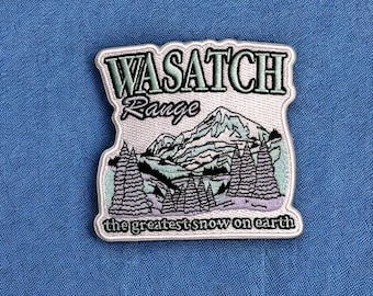 May include: Embroidered patch featuring the words "WASATCH Range" above a mountain scene with pine trees. The text "the greatest snow on earth" is at the bottom. The patch has a white border and is on a blue background.