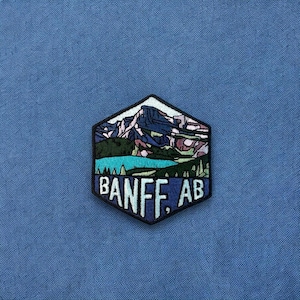 May include: A blue and green embroidered patch with a mountain range and a lake. The text "BANFF, AB" is below the image.