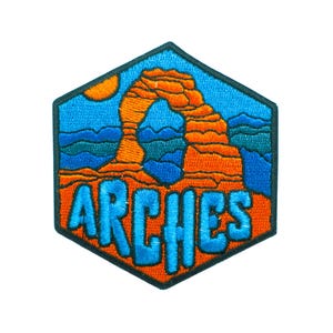 May include: Embroidered patch featuring the word "ARCHES" in blue, with an orange archway design and a yellow sun against a blue sky. The patch has a hexagonal shape with a dark green border.