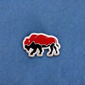 May include: A red and black embroidered patch of a bison, a common symbol of the American West.
