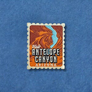 May include: Embroidered patch in the shape of a postage stamp featuring Antelope Canyon in Arizona. The design includes the text "Visit Antelope Canyon Arizona" in orange and white, with a canyon scene in shades of brown and a blue river.