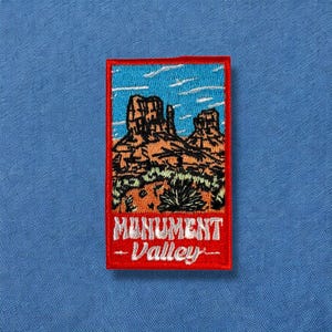 May include: Red embroidered patch with a blue sky and orange rock formations. The text "Monument Valley" is in white.