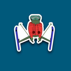 May include: A green frog wearing a red ski jacket and goggles is skiing down a snowy mountain. The frog is holding two ski poles and has a determined look on its face.