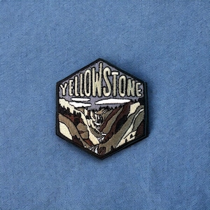 May include: A black and white embroidered patch with a landscape scene and the text "YELLOWSTONE" in white.