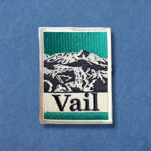 May include: A white and green embroidered patch with a mountain range and the word "Vail" in black lettering.