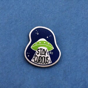 May include: A blue and green embroidered patch with a UFO and the text "STAY CURIOUS" in white.