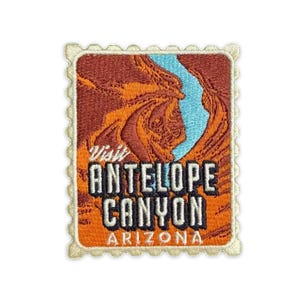 May include: Embroidered patch featuring a landscape of Antelope Canyon in Arizona. The design includes a blue river winding through orange and brown rock formations. The text "Visit Antelope Canyon Arizona" is displayed in white and orange.