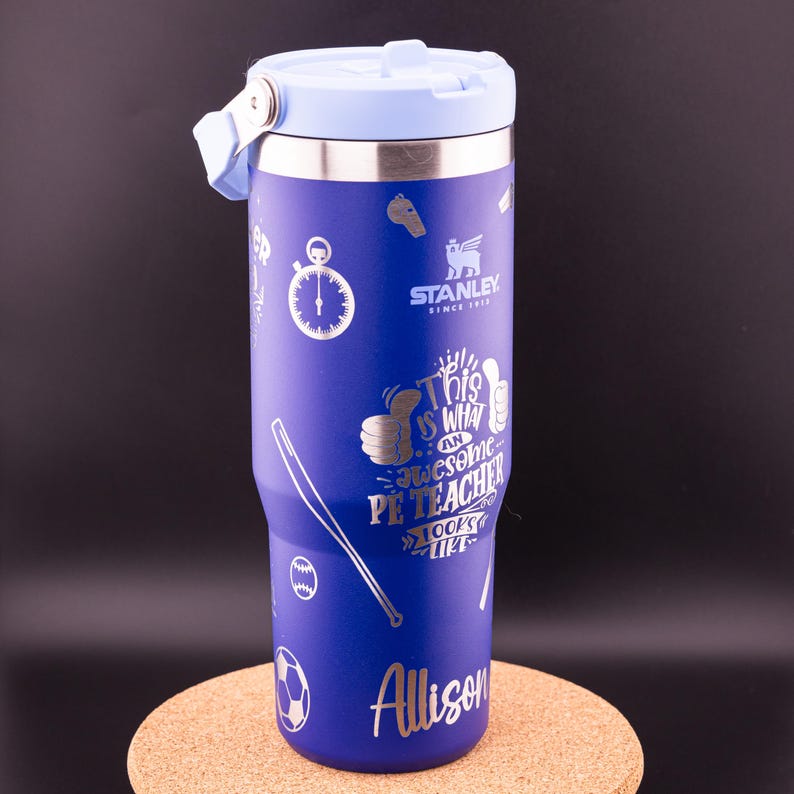 May include: A blue stainless steel travel mug with a silver lid and a silver inscription that reads "This is what an awesome PE Teacher looks like" and "Allison". The mug has a variety of sports-themed graphics, including a whistle, a stopwatch, a baseball bat, a baseball, a soccer ball, and a thumbs up.