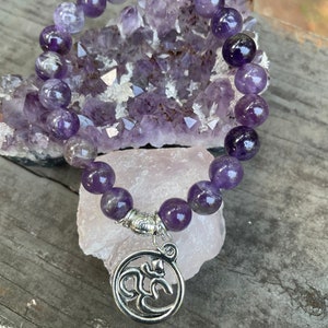 May include: Amethyst gemstone bracelet with a silver Om charm. The bracelet is made with round beads and has a stretchy elastic band.