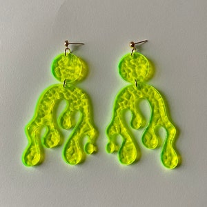 May include: A pair of neon green earrings with a dripping, abstract design. The earrings are made of acrylic and have a textured surface.