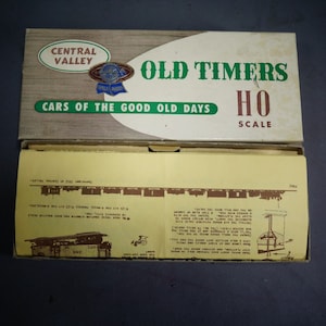 May include: A box for a model train set, featuring the text "Old Timers HO Scale Cars of the Good Old Days". The box is white with green and red accents. The box is open, revealing instructions for assembling the model train set.