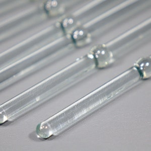 May include: Close-up of several clear glass stirring rods with rounded ends.