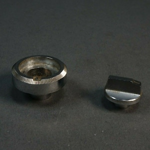 May include: Two silver-toned metal knobs, one round with a textured edge and the other a flat, rounded rectangle.