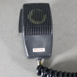 May include: A black microphone with a coiled cord and a Royce R label. The microphone has a black metal grille.