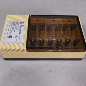 May include: A beige and brown Ni-Cd battery charger with a clear plastic top. The charger has four battery slots and a label that reads "NI-CD Battery Charger, Model: 21-1212, Input AC120V, Entree 60Hz 4W, Output DC2.7V, Sortie: 50mA max., Date: Jan-Mar 1990, Made in Hong Kong."