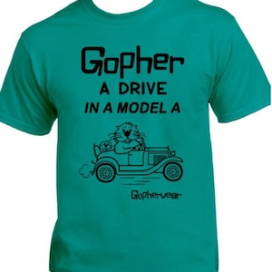May include: A teal blue t-shirt with a black graphic of a gopher driving a Model A car. The text on the shirt reads "Gopher a drive in a Model A" and "Gopherwear".