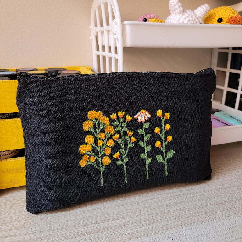 May include: Black canvas zippered pouch with embroidered yellow and white flowers. The flowers are stylized and have a simple design.