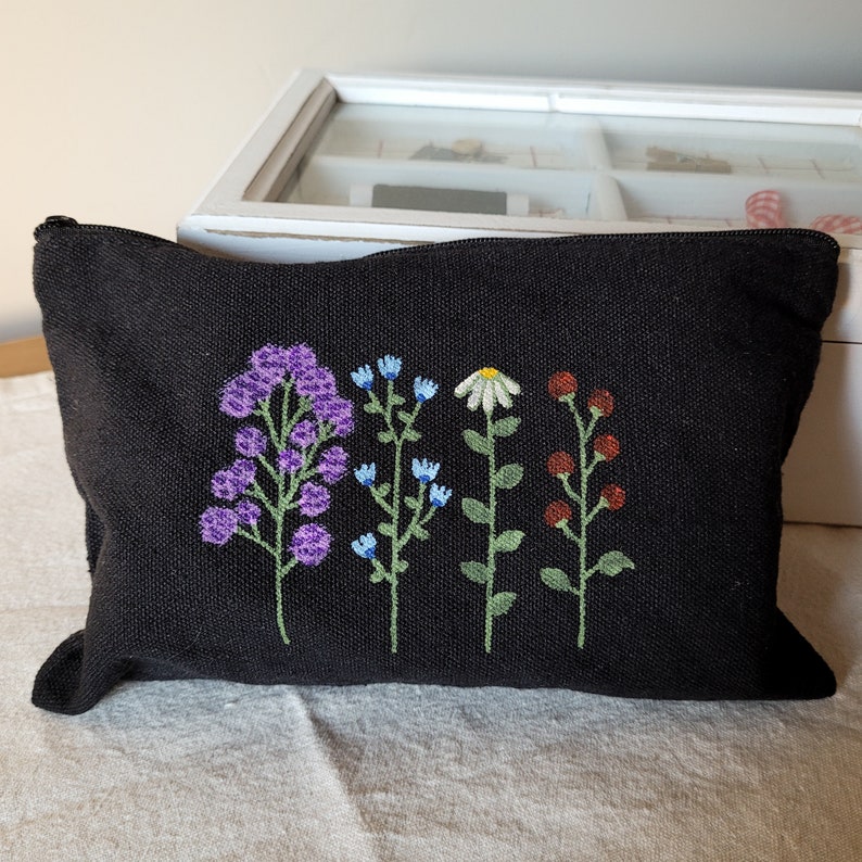 May include: Black canvas zippered pouch with embroidered flowers in shades of purple, blue, white, green, and red.