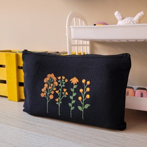 May include: Black canvas zippered pouch with embroidered yellow and orange flowers.