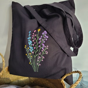 Puede incluir: Bolsa de lona negra con un diseño floral bordado de colores. Las flores son rosas, azules, amarillas y verdes.