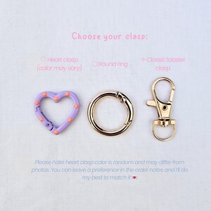 May include: Image of three clasp options: a heart-shaped clasp in lavender with orange dots, a gold round ring clasp, and a gold classic lobster clasp. Text reads "Choose your clasp:" and additional text about color variations.