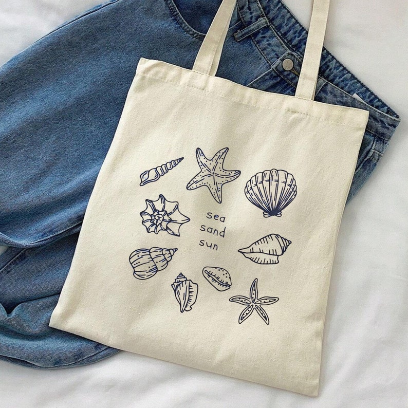 May include: A beige canvas tote bag with a blue outline of seashells, starfish, and the words "sea sand sun".