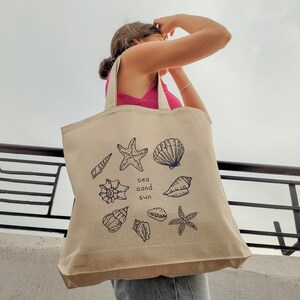 May include: A beige tote bag with a blue and white design of seashells, starfish, and the words "sea sand sun".