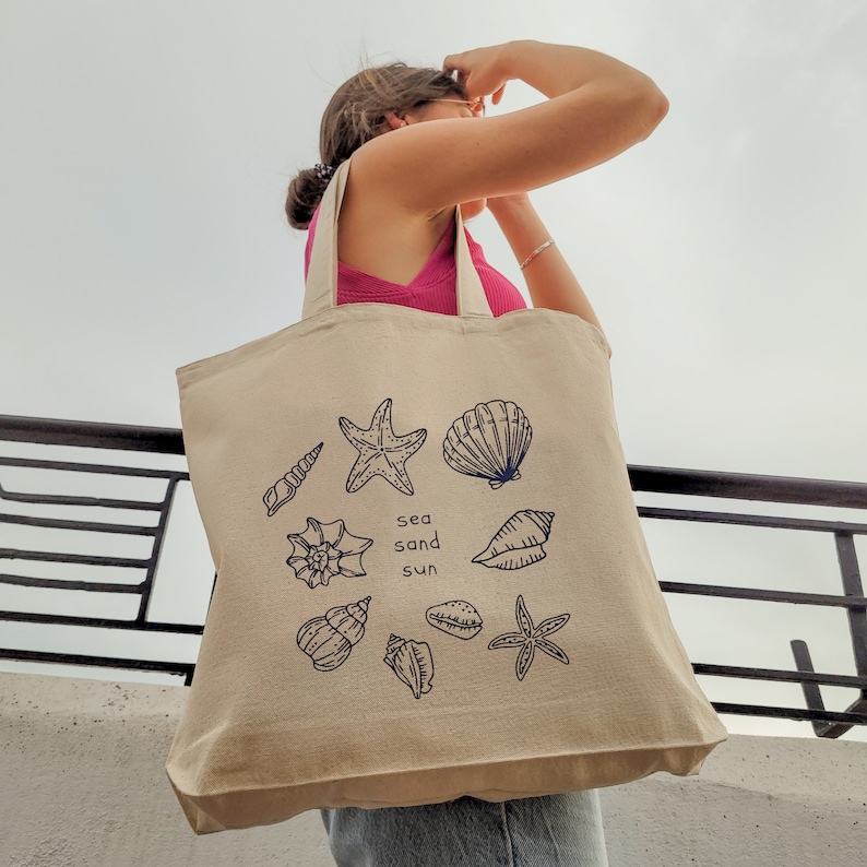 May include: A beige tote bag with a blue and white design of seashells, starfish, and the words "sea sand sun".