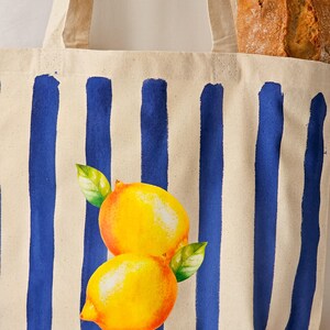 May include: A white canvas tote bag with blue stripes and a yellow lemon design. The bag has two handles.