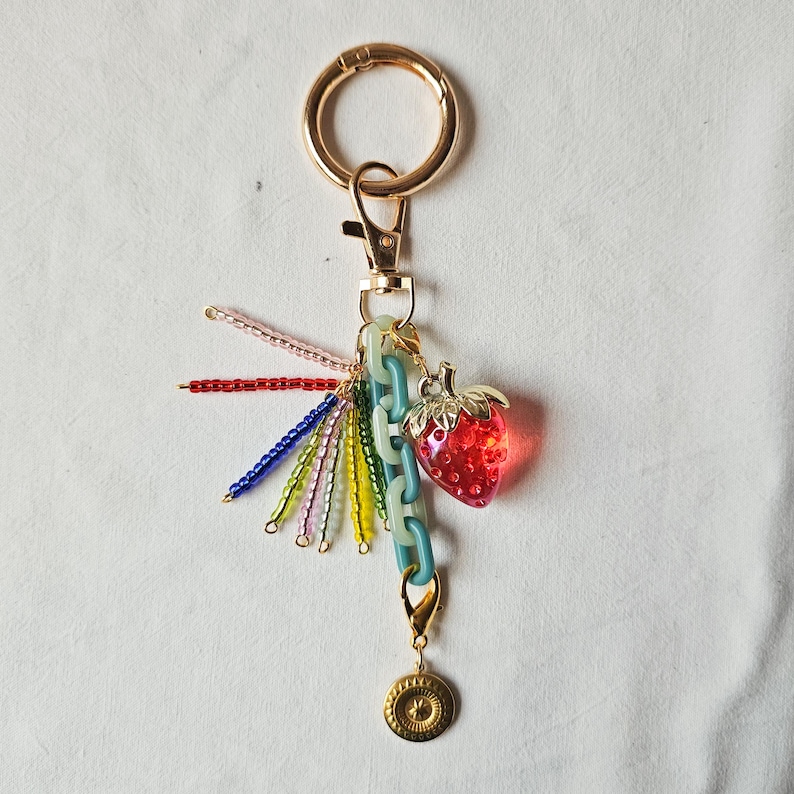 May include: A gold key chain with a colorful beaded tassel and a red and clear plastic strawberry charm.