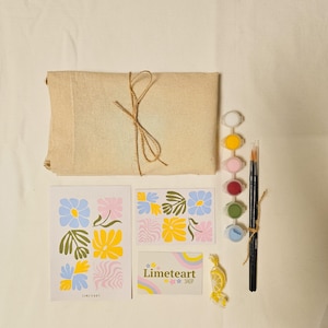 May include: A paint-by-numbers kit with a beige canvas-wrapped package tied with twine, paint pots, brushes, and floral design cards. The cards feature blue, yellow, and pink flowers. A small card reads "Limeteart Shop."