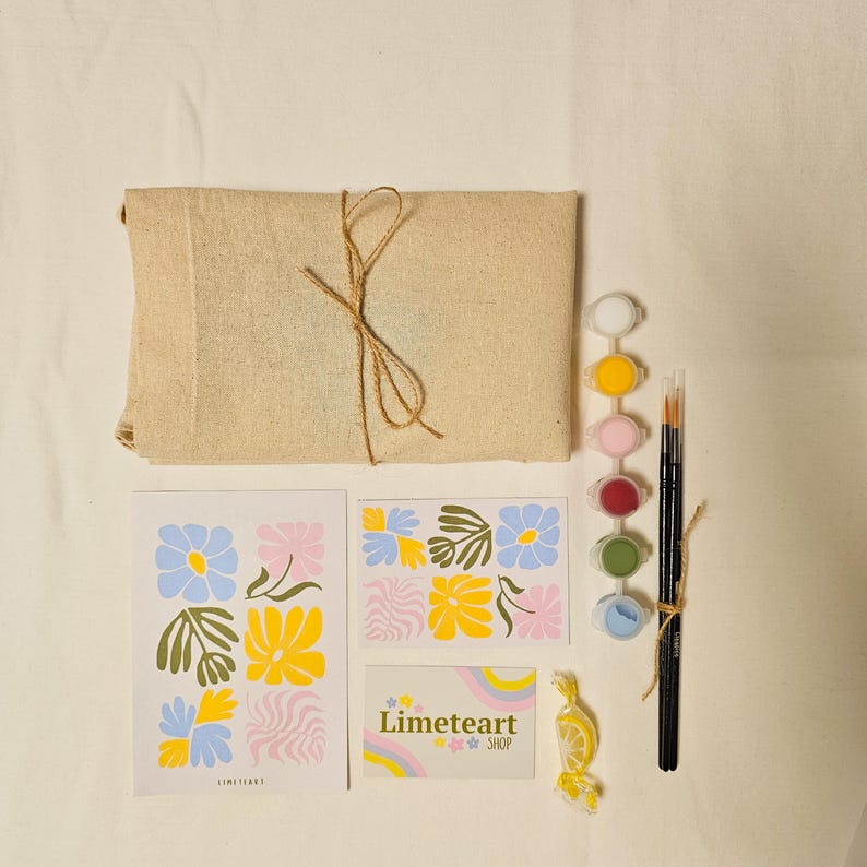 May include: A paint-by-numbers kit with a beige canvas-wrapped package tied with twine, paint pots, brushes, and floral design cards. The cards feature blue, yellow, and pink flowers. A small card reads "Limeteart Shop."