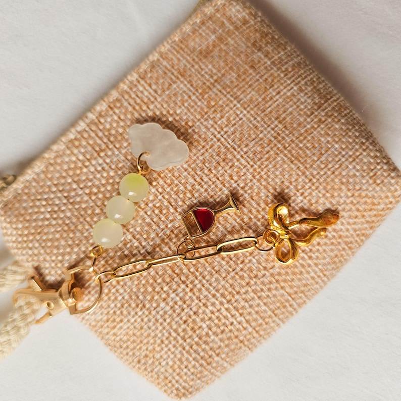 Puede incluir: Un brazalete de charms de oro con una variedad de charms, incluyendo una copa de vino, una nube y un lazo. Los charms est&aacute;n unidos a una cadena de oro y un cierre de langosta.