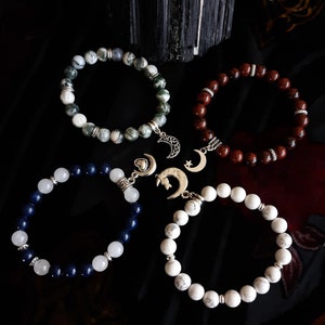 May include: Four bracelets with silver moon and star charms. The bracelets are made of different stones: green and white agate, red jasper, blue lapis lazuli, and white howlite.