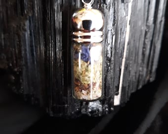 May include: A silver chain necklace with a glass vial pendant filled with dried herbs and flowers. The vial has a silver cap and is suspended from a silver chain.