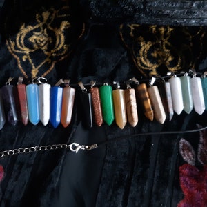 May include: A necklace with a variety of gemstone pendants in different colors and shapes. The pendants are attached to a black cord and a silver chain.